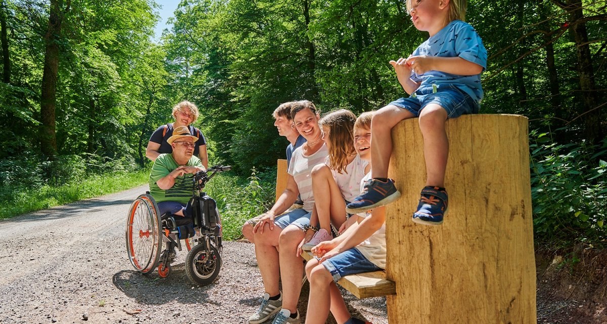 Menschen sitzen und stehen auf einem Waldweg, darunter ein Mann im Rollstuhl. Sie lachen und genießen die Natur., © Natur.Nah. Schönbuch & Heckengäu Menschen sitzen und stehen auf einem Waldweg, darunter ein Mann im Rollstuhl. Sie lachen und genießen die Natur., © Natur.Nah. Schönbuch & Heckengäu