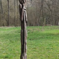 Eine abstrakte Holzskulptur steht auf einer grünen Wiese, umgeben von kahlen Bäumen und einem steinernen Hintergrund., © Natur.Nah. Schönbuch & Heckengäu
