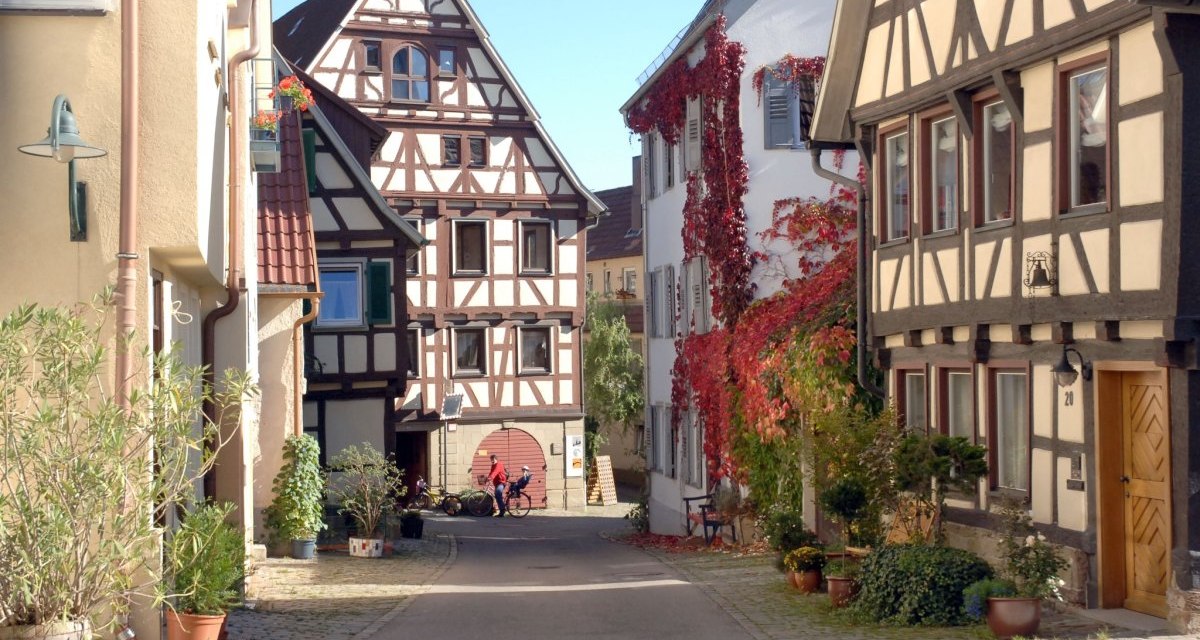 Enge Gasse mit Fachwerkhäusern, roten Weinreben an den Wänden und Pflanzen in Töpfen. Zwei Personen mit Fahrrädern im Hintergrund., © Stadt Herrenberg Enge Gasse mit Fachwerkhäusern, roten Weinreben an den Wänden und Pflanzen in Töpfen. Zwei Personen mit Fahrrädern im Hintergrund., © Stadt Herrenberg
