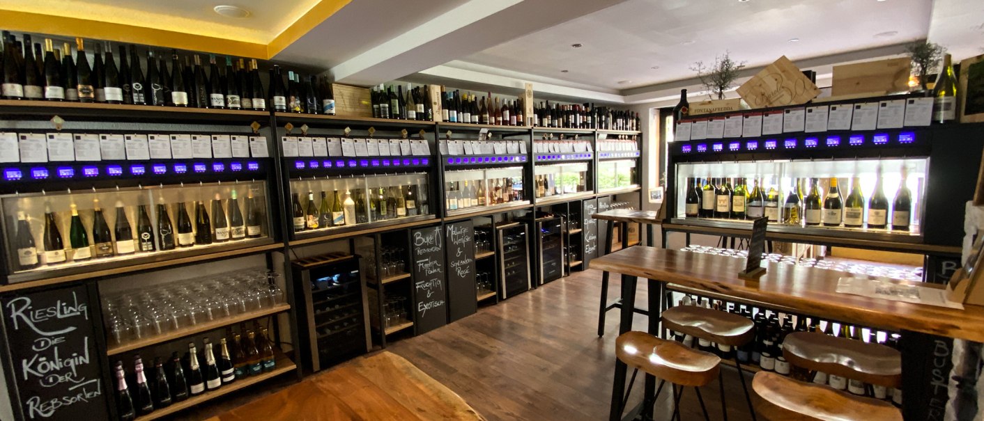 Weinladen mit Regalen voller Weinflaschen, Verkostungstischen und Gläsern. Moderne Einrichtung mit Holz- und Metallelementen., © Sitt-Wein Weinladen mit Regalen voller Weinflaschen, Verkostungstischen und Gläsern. Moderne Einrichtung mit Holz- und Metallelementen., © Sitt-Wein