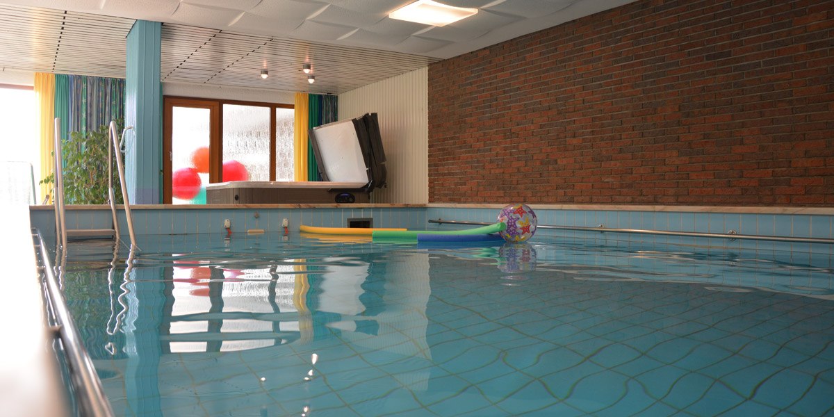 Innenpool mit blauen Fliesen, bunten Schwimmnudeln und einem Ball. Fenster mit Vorhängen und Backsteinwand im Hintergrund., © Hotel Hochwald