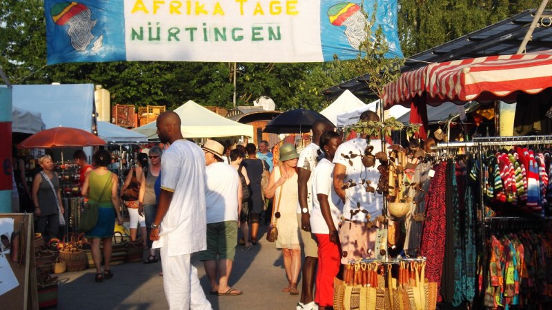 Besucher schlendern &uuml;ber die Afrika Tage N&uuml;rtingen, umgeben von bunten Marktst&auml;nden und einem Banner im Hintergrund., &copy; Stadt N&uuml;rtingen