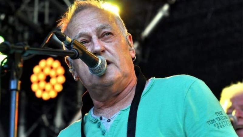 Ein Mann in einem grünen Shirt singt in ein Mikrofon auf einer Bühne. Im Hintergrund sind Lichter und Bühnenequipment zu sehen., © Interessengemeinschaft Kultur Sindelfingen / Böblingen e.V.