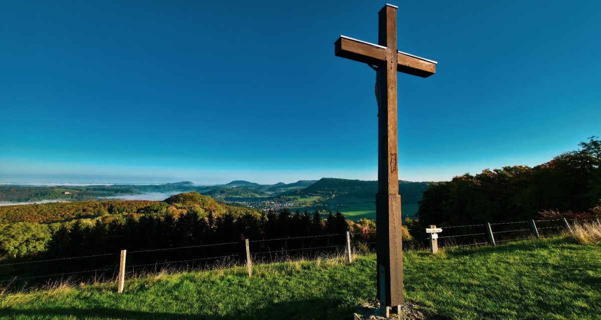 Holzkreuz auf Wiese mit Blick auf hügelige Landschaft und blauem Himmel., © Landkreis Göppingen Holzkreuz auf Wiese mit Blick auf hügelige Landschaft und blauem Himmel., © Landkreis Göppingen