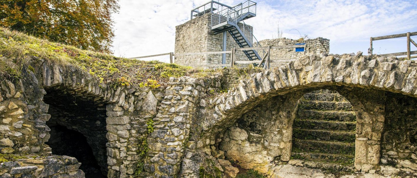 Die Burgruine Hiltenburg in Bad Ditzenbach zeigt alte Steinbögen und Treppen, umgeben von herbstlichem Laub und einem klaren Himmel., © SMG, Sarah Schmid Die Burgruine Hiltenburg in Bad Ditzenbach zeigt alte Steinbögen und Treppen, umgeben von herbstlichem Laub und einem klaren Himmel., © SMG, Sarah Schmid