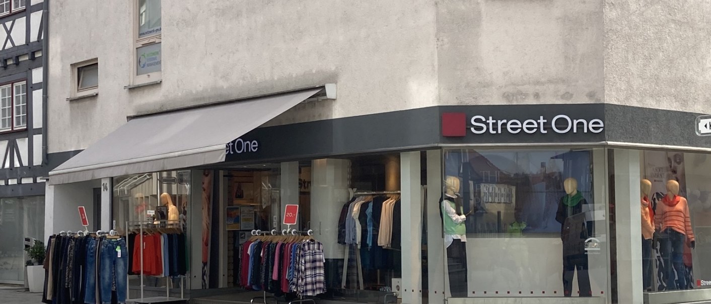 Außenansicht des "Street One" Partner Stores in Nürtingen mit Schaufenstern und Kleidung auf Ständern vor dem Geschäft., © Lena Besemer Außenansicht des "Street One" Partner Stores in Nürtingen mit Schaufenstern und Kleidung auf Ständern vor dem Geschäft., © Lena Besemer