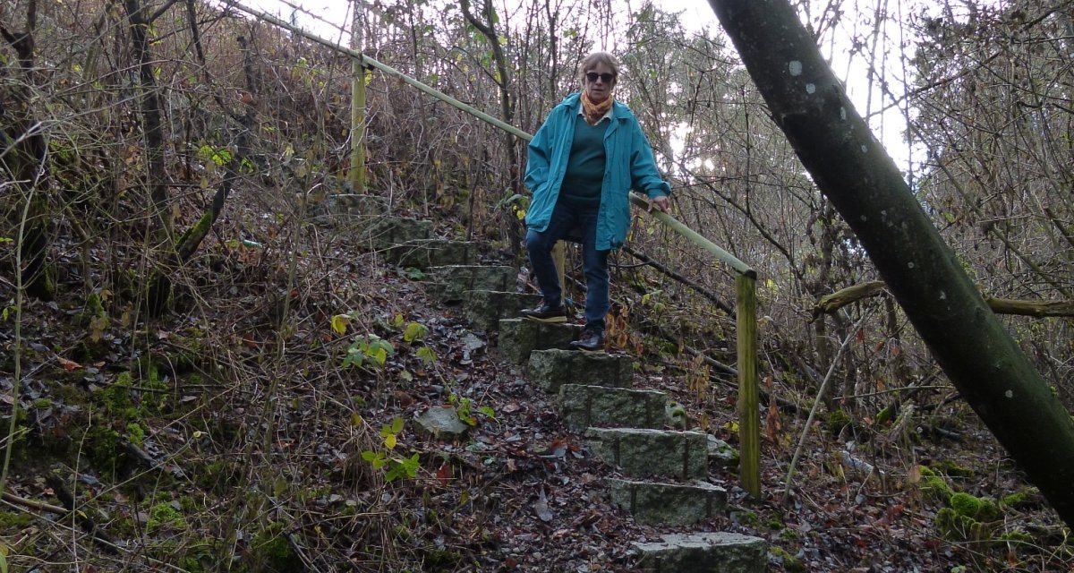 Eine Person in blauer Jacke steigt eine steinige Treppe in einem bewaldeten Gebiet hinab. Die Umgebung ist herbstlich und karg., © Natur.Nah. Schönbuch & Heckengäu Eine Person in blauer Jacke steigt eine steinige Treppe in einem bewaldeten Gebiet hinab. Die Umgebung ist herbstlich und karg., © Natur.Nah. Schönbuch & Heckengäu