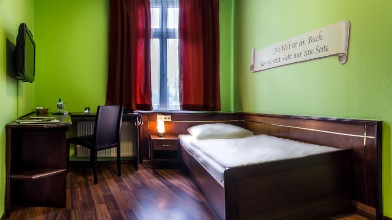 Ein gemütliches Einzelzimmer mit grün gestrichenen Wänden, einem Einzelbett, Schreibtisch und Stuhl. Ein roter Vorhang hängt am Fenster., © TOMAS Ein gemütliches Einzelzimmer mit grün gestrichenen Wänden, einem Einzelbett, Schreibtisch und Stuhl. Ein roter Vorhang hängt am Fenster., © TOMAS