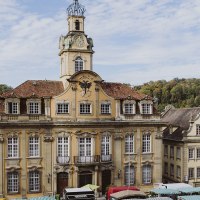 Historisches Gebäude in Schwäbisch Hall mit Marktständen davor, umgeben von weiteren alten Gebäuden und Bäumen im Hintergrund., © Nico Kurth