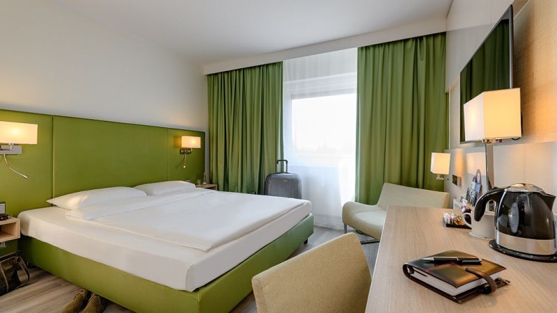 Modernes Doppelzimmer mit grünem Kopfteil, Schreibtisch, Wasserkocher und großem Fenster mit grünen Vorhängen., © Mercure Bristol Stuttgart Sindelfingen Modernes Doppelzimmer mit grünem Kopfteil, Schreibtisch, Wasserkocher und großem Fenster mit grünen Vorhängen., © Mercure Bristol Stuttgart Sindelfingen
