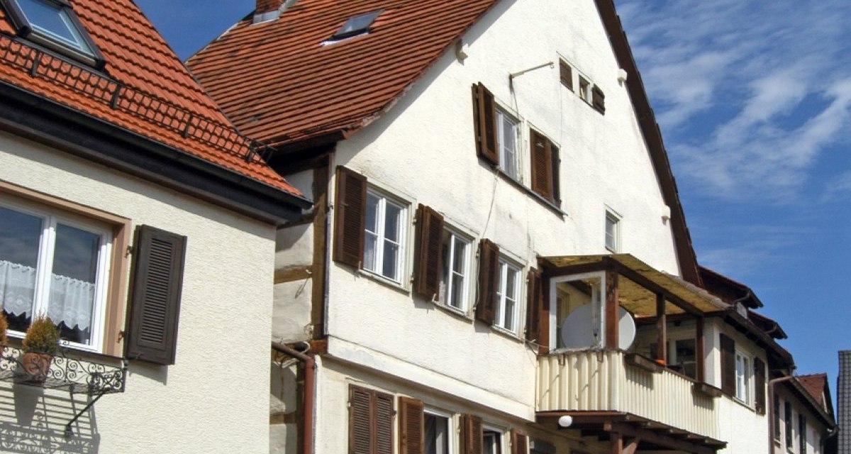 Traditionelles Fachwerkhaus mit rotem Ziegeldach, Holzfensterl&auml;den und kleinem Balkon. Ein rotes Auto steht davor, blauer Himmel im Hintergrund., &copy; Natur.Nah. Sch&ouml;nbuch & Heckeng&auml;u