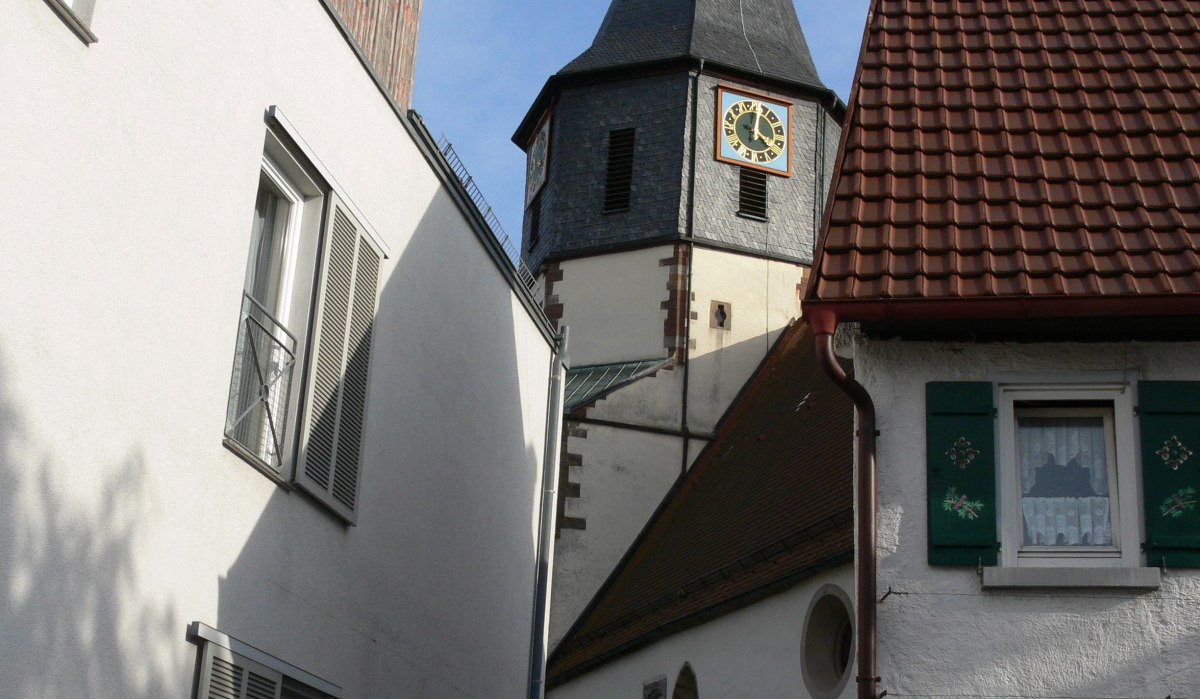 Spitzer Kirchturm der evangelischen Pfarrkirche St. Clemens ragt zwischen weißen Wohnhäusern hervor, blauer Himmel im Hintergrund., © Land der 1000 Hügel - Kraichgau-Stromberg Spitzer Kirchturm der evangelischen Pfarrkirche St. Clemens ragt zwischen weißen Wohnhäusern hervor, blauer Himmel im Hintergrund., © Land der 1000 Hügel - Kraichgau-Stromberg
