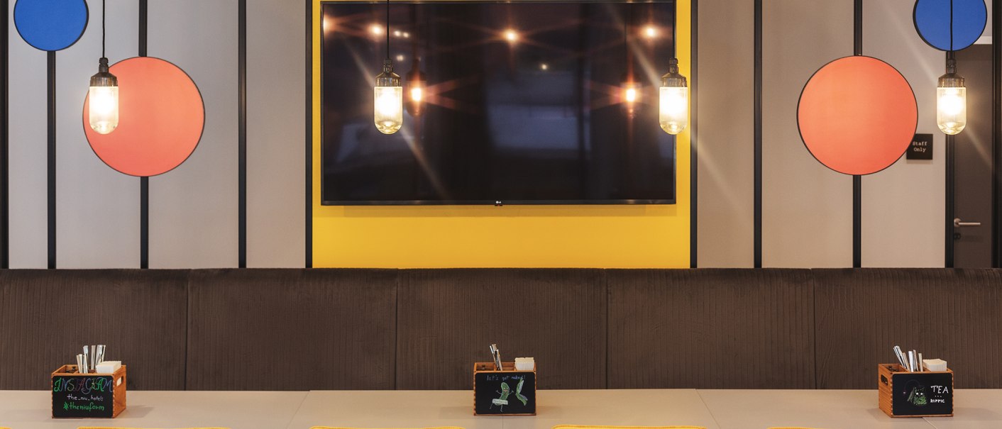 Modernes Restaurant mit bunten Kreisen an der Wand, hängenden Lampen und Tischen mit Besteckboxen., © the niu Form - Novum Hospitality