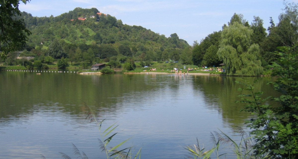 Ein See mit ruhigem Wasser, umgeben von gr&uuml;nen H&uuml;geln und B&auml;umen. Menschen entspannen am Ufer., &copy; Remstal Tourismus e.V.
