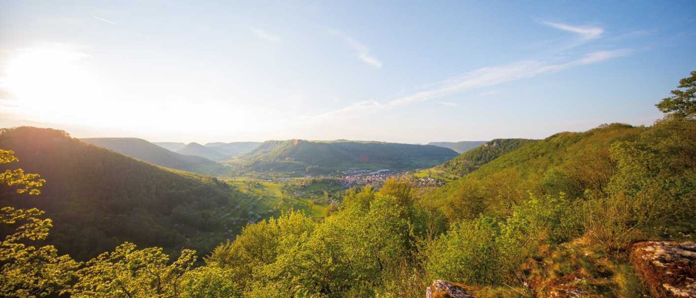 Panoramablick auf grüne Hügel und ein Tal mit einem Dorf. Die Sonne scheint von links, der Himmel ist klar mit wenigen Wolken., © SMG, Achim Mende Panoramablick auf grüne Hügel und ein Tal mit einem Dorf. Die Sonne scheint von links, der Himmel ist klar mit wenigen Wolken., © SMG, Achim Mende