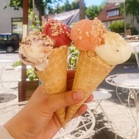 Drei Eiswaffeln mit verschiedenen Eissorten und N&uuml;ssen, gehalten von einer Hand unter einem Sonnenschirm im Freien., &copy; E. Dogan