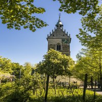 Ein Kirchturm in Fellbach ragt zwischen grünen Bäumen empor, unter einem klaren blauen Himmel. Die Umgebung wirkt friedlich und einladend., © SMG, Sarah Schmid