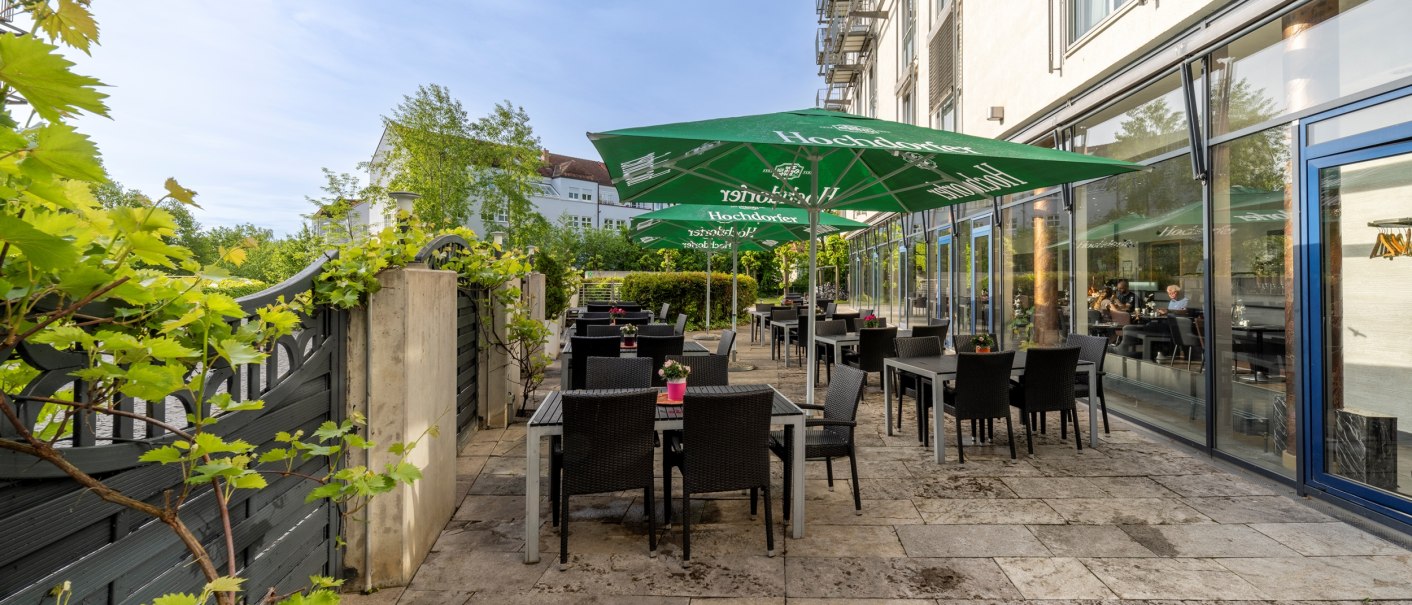 Eine Terrasse mit schwarzen Tischen und Stühlen, grünen Sonnenschirmen und Pflanzen an einem sonnigen Tag., © Plaza Residence Stuttgart-Ditzingen Eine Terrasse mit schwarzen Tischen und Stühlen, grünen Sonnenschirmen und Pflanzen an einem sonnigen Tag., © Plaza Residence Stuttgart-Ditzingen