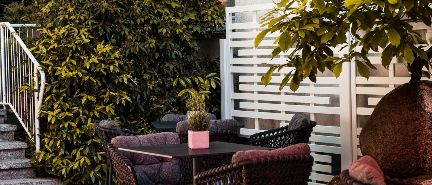 Gemütliche Terrasse mit geflochtenen Stühlen, Tisch, Pflanzen und einem weißen Sichtschutz. Eine Treppe führt zur Terrasse., © Ringhotel Adler Asperg