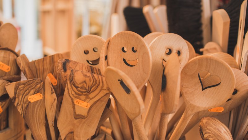 Holzlöffel mit lachenden Gesichtern und Herzmotiv auf einem Marktstand. Verschiedene Holzarten und Preisschilder sind sichtbar., © Stadt Schorndorf