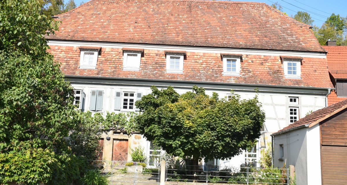 Ein ehemaliges Bauernhaus mit Fachwerk und rotem Ziegeldach, umgeben von B&auml;umen und Pflanzen. Der Eingangsbereich ist von Gr&uuml;n umrahmt., &copy; Land der 1000 H&uuml;gel - Kraichgau-Stromberg