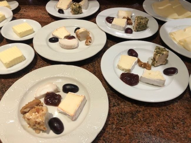 Mehrere Teller mit verschiedenen Käsesorten, Trauben, Walnüssen und Marmelade auf einem braunen Tisch arrangiert., © Kronen Hotel GmbH Mehrere Teller mit verschiedenen Käsesorten, Trauben, Walnüssen und Marmelade auf einem braunen Tisch arrangiert., © Kronen Hotel GmbH