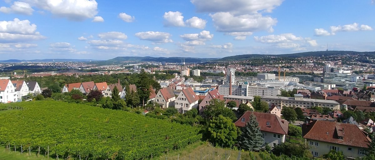 Blick auf Stuttgart mit Weinbergen im Vordergrund, Wohnh&auml;usern und der Stadt im Hintergrund unter blauem Himmel mit Wolken., &copy; Stuttgart-Marketing GmbH