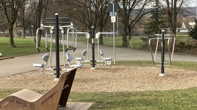 Ein Outdoor-Fitnessbereich mit verschiedenen Trainingsger&auml;ten und einer Holzbank in einem Park. Die Umgebung ist von B&auml;umen umgeben., &copy; StadtN&uuml;rtingen