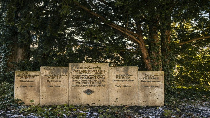 Steintafeln im Kurpark von Bad Überkingen informieren über verschiedene Quellen, umgeben von Bäumen und Efeu., © SMG, Sarah Schmid Steintafeln im Kurpark von Bad Überkingen informieren über verschiedene Quellen, umgeben von Bäumen und Efeu., © SMG, Sarah Schmid