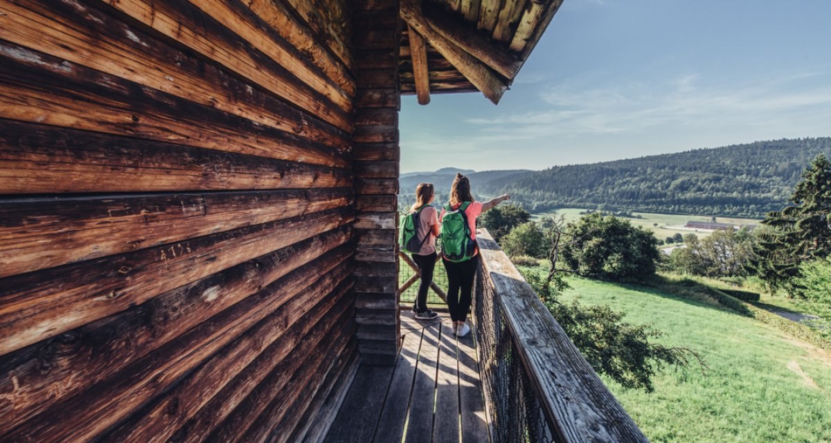 Zwei Personen mit Rucksäcken stehen auf einem Holzbalkon und schauen in die grüne Landschaft. Der Himmel ist klar und blau., © Tourismus Ostalb Zwei Personen mit Rucksäcken stehen auf einem Holzbalkon und schauen in die grüne Landschaft. Der Himmel ist klar und blau., © Tourismus Ostalb