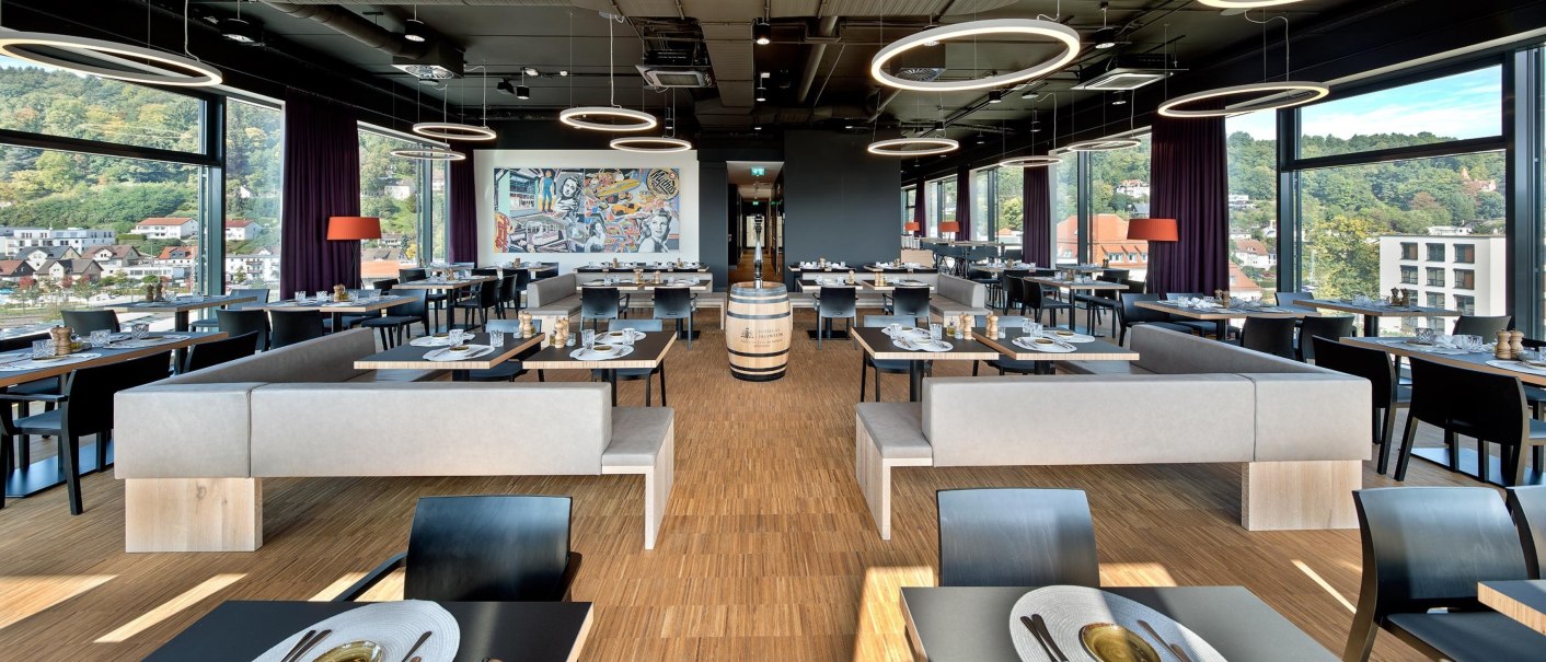 Modernes Restaurant im 7. Stock mit großen Fenstern, stilvollen Möbeln und einem Wandgemälde. Helle Beleuchtung und Aussicht auf die Stadt., © Hotel am Remspark Modernes Restaurant im 7. Stock mit großen Fenstern, stilvollen Möbeln und einem Wandgemälde. Helle Beleuchtung und Aussicht auf die Stadt., © Hotel am Remspark