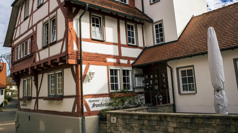 Fachwerkhaus mit Schild "Ristorante Pizzeria Storchennest". Ein geschlossener Sonnenschirm steht davor. Im Hintergrund sind weitere Geb&auml;ude zu sehen., &copy; Stuttgart Marketing GmbH, Sarah Schmid