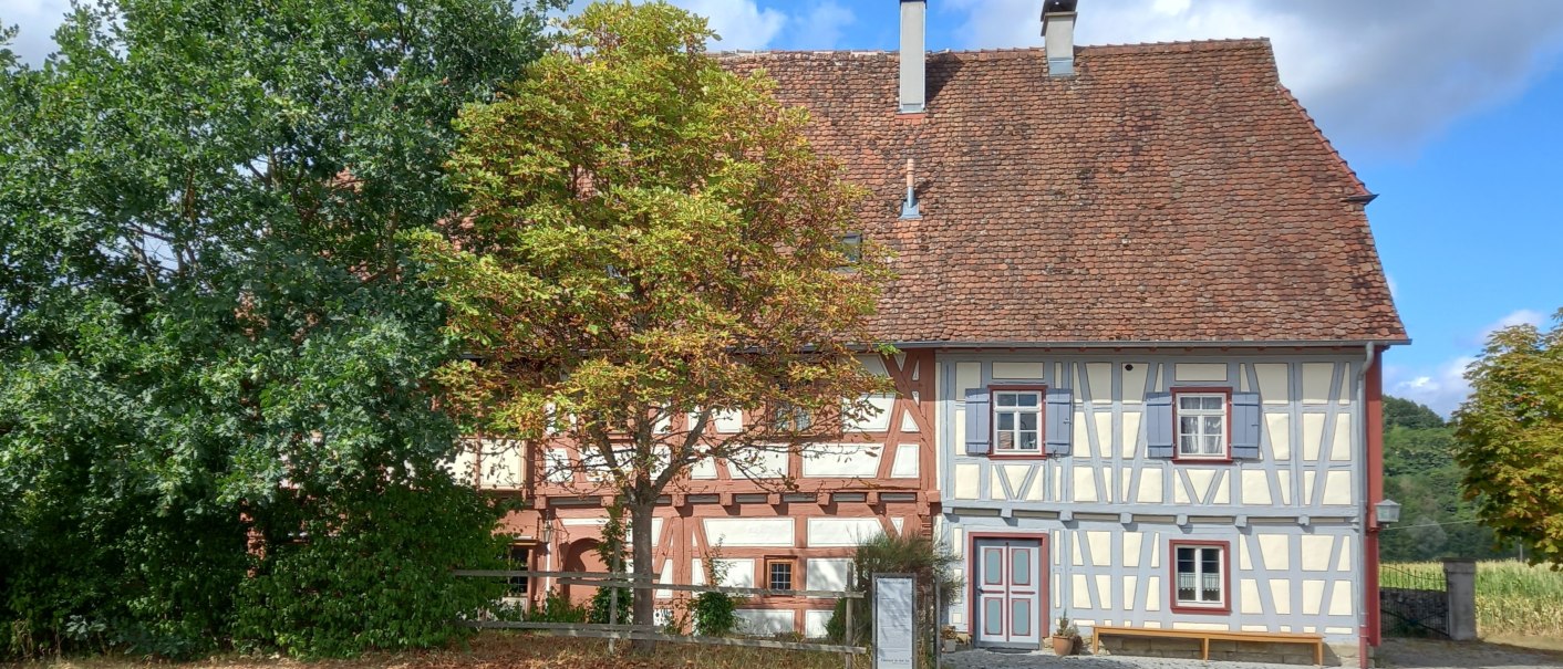 Zweigeteiltes Fachwerkhaus - linke Haush&auml;lfte mit rotem Fachwerk und hellesn Gefachen, rechte Haush&auml;lfte mit hellgrauem Fachwerk. Das Geb&auml;ude hat ein rotes Ziegeldach und ist von B&auml;umen umgeben., &copy; Petra Natzkowski