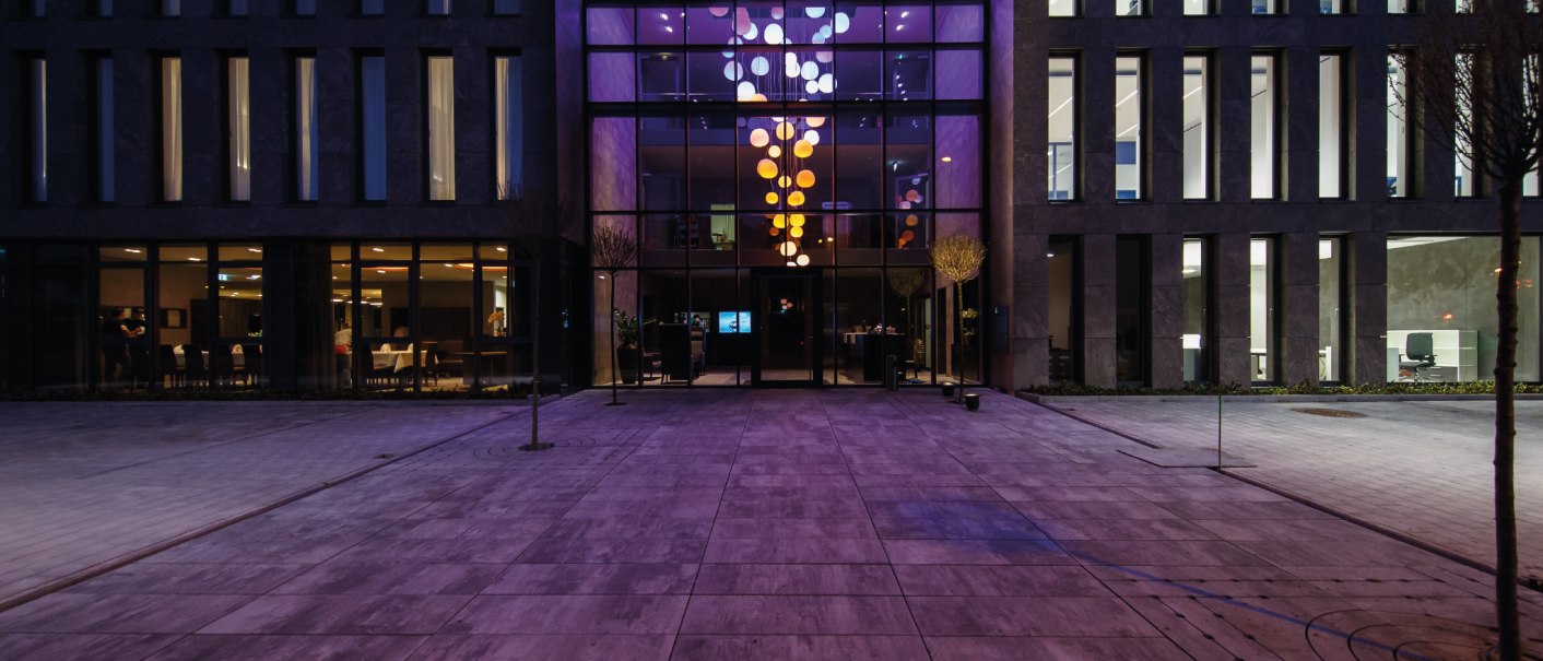 Moderne Gebäudeaußenansicht bei Nacht. Große Fenster und lila Beleuchtung im Eingangsbereich. Symmetrische Architektur mit klaren Linien., © Hotel Eislinger Tor