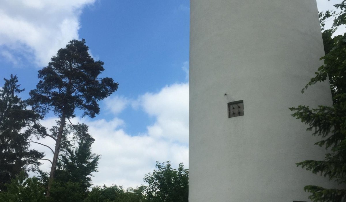 Weißer Turm neben Bäumen, blauer Himmel mit Wolken, Holztisch im Vordergrund., © www.pro-cycl.de Weißer Turm neben Bäumen, blauer Himmel mit Wolken, Holztisch im Vordergrund., © www.pro-cycl.de