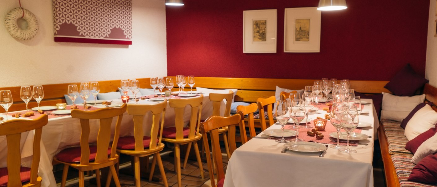 Gemütlich gedeckter Tisch in einem Restaurant mit Weingläsern, Kerzen und Holzmöbeln. Die Wände sind rot und weiß dekoriert., © 70469R! Weinbau Fabian Rajtschan