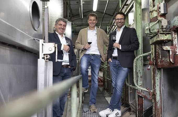 Drei Männer stehen in einer Weinkelterei, lächelnd mit Weingläsern in der Hand. Sie tragen legere, aber schicke Kleidung., © Esslinger Stadtmarketing &amp; Tourismus GmbH