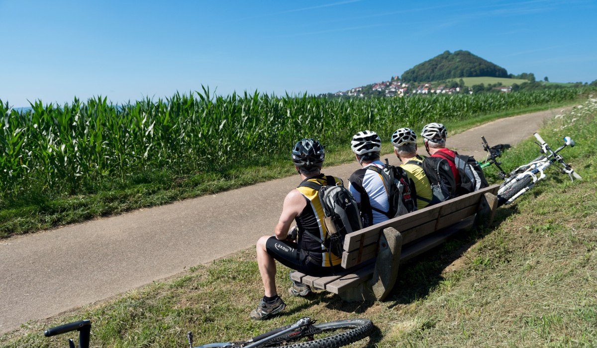 Drei Radfahrer mit Helmen sitzen auf einer Bank am Wegesrand, Fahrräder liegen daneben. Im Hintergrund ist der Hohenstaufen zu sehen., © Landkreis Göppingen Drei Radfahrer mit Helmen sitzen auf einer Bank am Wegesrand, Fahrräder liegen daneben. Im Hintergrund ist der Hohenstaufen zu sehen., © Landkreis Göppingen