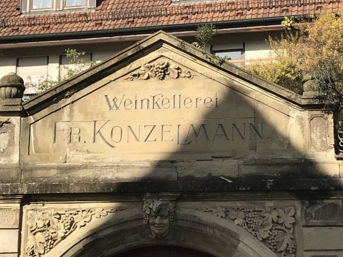 Steinportal der Weinkellerei Fr. Konzelmann mit dekorativen Weinreben und Gesichtsskulptur, im Hintergrund ein Geb&auml;ude mit Ziegeldach., &copy; Weingenuss Stuttgart
