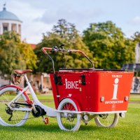 Ein rotes Lastenfahrrad mit der Aufschrift 'I-Bike' steht auf einer Wiese vor einem Brunnen und einem Gebäude mit Kuppel., © Stuttgart-Marketing GmbH, Thomas Niedermüller Ein rotes Lastenfahrrad mit der Aufschrift 'I-Bike' steht auf einer Wiese vor einem Brunnen und einem Gebäude mit Kuppel., © Stuttgart-Marketing GmbH, Thomas Niedermüller
