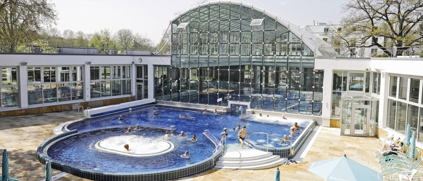 Das SoleBad Bad Cannstatt zeigt ein modernes Schwimmbecken mit Glasfassade. Menschen entspannen im Wasser und auf Liegestühlen., © Stuttgarter Bäder Das SoleBad Bad Cannstatt zeigt ein modernes Schwimmbecken mit Glasfassade. Menschen entspannen im Wasser und auf Liegestühlen., © Stuttgarter Bäder