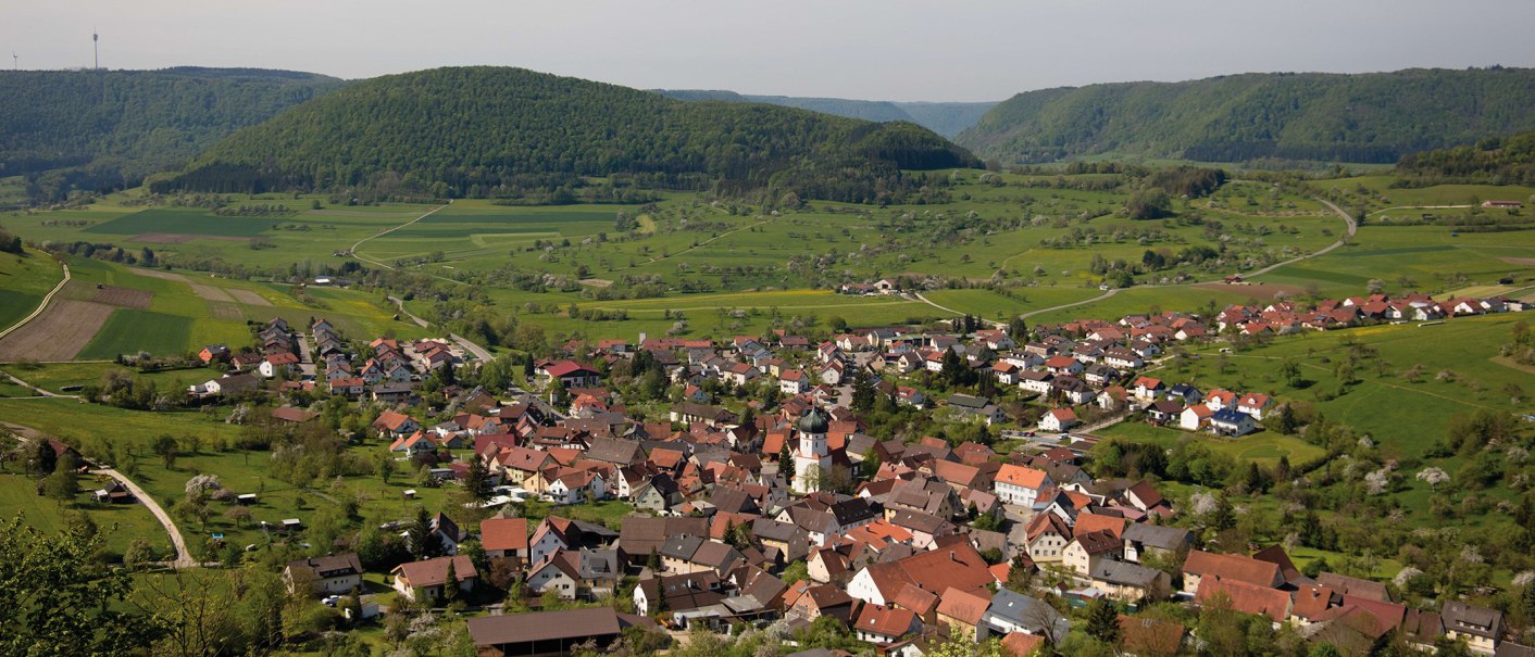 Luftaufnahme von Bad Überkingen, umgeben von grünen Hügeln und Feldern. Die Stadt zeigt rote und braune Dächer, eingebettet in eine ländliche Landschaft., © Stuttgart-Marketing GmbH, Achim Mende
