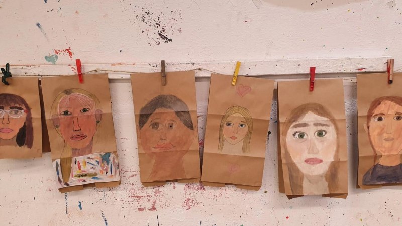 Sechs gemalte Selbstportraits von Kindern auf braunem Papier, aufgehängt mit bunten Wäscheklammern an einer weißen, bemalten Wand., © Kunstschule Labyrinth Sechs gemalte Selbstportraits von Kindern auf braunem Papier, aufgehängt mit bunten Wäscheklammern an einer weißen, bemalten Wand., © Kunstschule Labyrinth