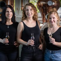 Drei Frauen in schwarzer Kleidung stehen in einer Brauerei und halten Gläser mit Getränken. Im Hintergrund sind Brauereigeräte zu sehen., © Brau- & Brennwerkstatt Drei Frauen in schwarzer Kleidung stehen in einer Brauerei und halten Gläser mit Getränken. Im Hintergrund sind Brauereigeräte zu sehen., © Brau- & Brennwerkstatt