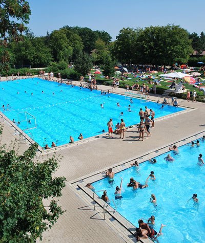 Zwei Schwimmbecken im Waldfreibad Holzgerlingen, umgeben von Bäumen und Liegewiesen. Viele Menschen schwimmen und entspannen sich in der Sonne., © Stadt Holzgerlingen Zwei Schwimmbecken im Waldfreibad Holzgerlingen, umgeben von Bäumen und Liegewiesen. Viele Menschen schwimmen und entspannen sich in der Sonne., © Stadt Holzgerlingen