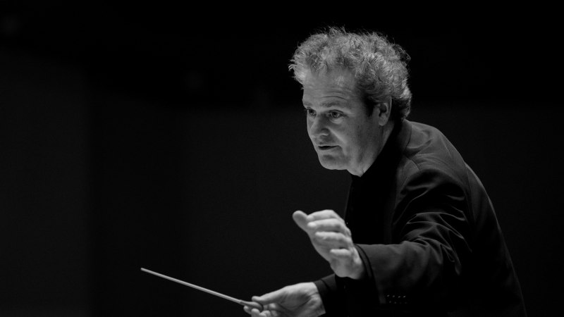 Ein Dirigent in Aktion, hält einen Taktstock in der Hand. Schwarz-weiß Foto mit Fokus auf seine konzentrierte Mimik., © Ines Fuchs Ein Dirigent in Aktion, hält einen Taktstock in der Hand. Schwarz-weiß Foto mit Fokus auf seine konzentrierte Mimik., © Ines Fuchs