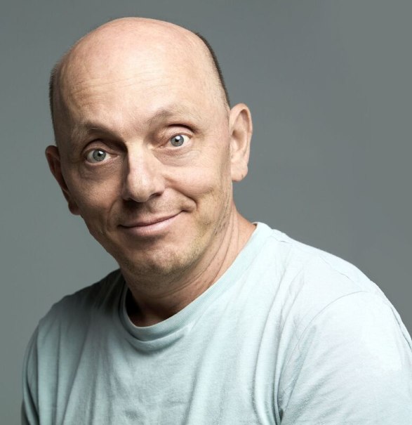 Ein Mann mit Glatze und hellem T-Shirt l&auml;chelt in die Kamera. Der Hintergrund ist grau und schlicht gehalten., &copy; Stadthalle Leonberg