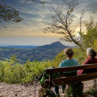 Zwei Personen sitzen auf einer Bank am Aussichtspunkt Luginsland und genießen den Blick auf die hügelige Landschaft im Sonnenuntergang., © Foto: Mario Klaiber Zwei Personen sitzen auf einer Bank am Aussichtspunkt Luginsland und genießen den Blick auf die hügelige Landschaft im Sonnenuntergang., © Foto: Mario Klaiber