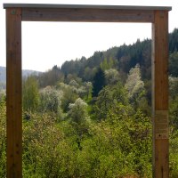 Ein Holzrahmen steht vor einer grünen, bewaldeten Landschaft am Venusberg. Blühende Bäume und Hügel sind im Hintergrund sichtbar., © Natur.Nah. Schönbuch & Heckengäu