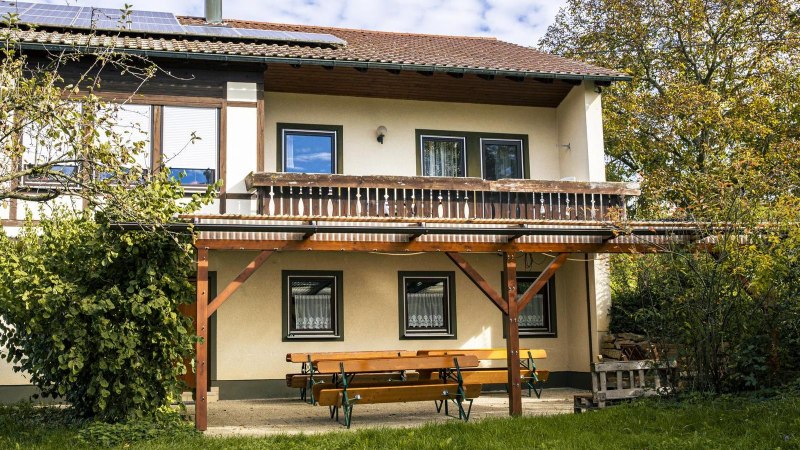 Zweistöckiges Gebäude mit Balkon, Solarpanelen auf dem Dach, umgeben von Bäumen. Eine Holzbank steht davor., © Stuttgart Marketing GmbH, Sarah Schmid